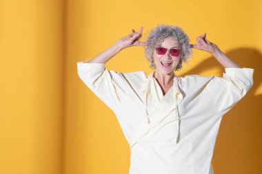 Sarı arka planda poz veren bir kadın komik surat yapıyor.