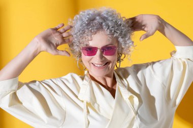 Pembe güneş gözlüklü olgun bir kadın gülümsüyor.