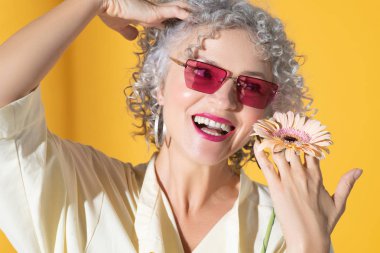 Pembe gözlüklü kıvırcık kadın elinde çiçekle