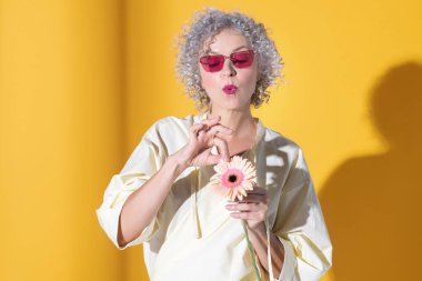 Sarı arka planda küçük bir çiçekle poz veren kadın