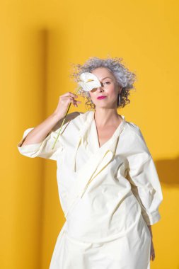 Gri saçlı, kıvırcık saçlı, çiçekle poz veren kadın.