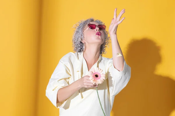 Mulher soprando em pétalas enquanto posando com flor — Fotografia de Stock