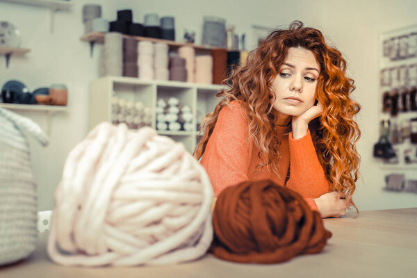 Thoughtful red haired female looking at yarn