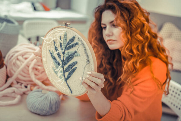 Charming red haired girl looking at her lace-frame