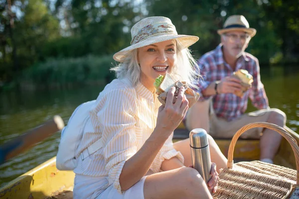 Beautiful wife eating sandwich while sitting in boat with husband — Stock Photo, Image