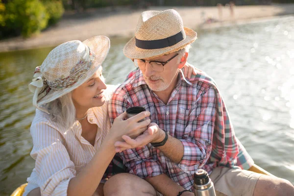 Esposa con sombrero de verano dando un poco de té a su marido —  Fotos de Stock