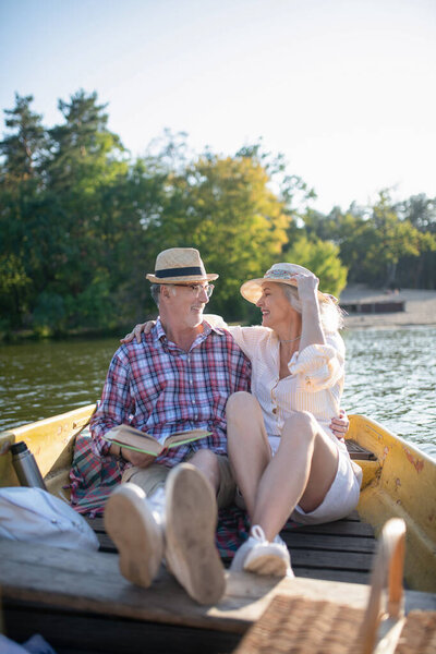 Senior adults sitting in boat and reading book while enjoying evening