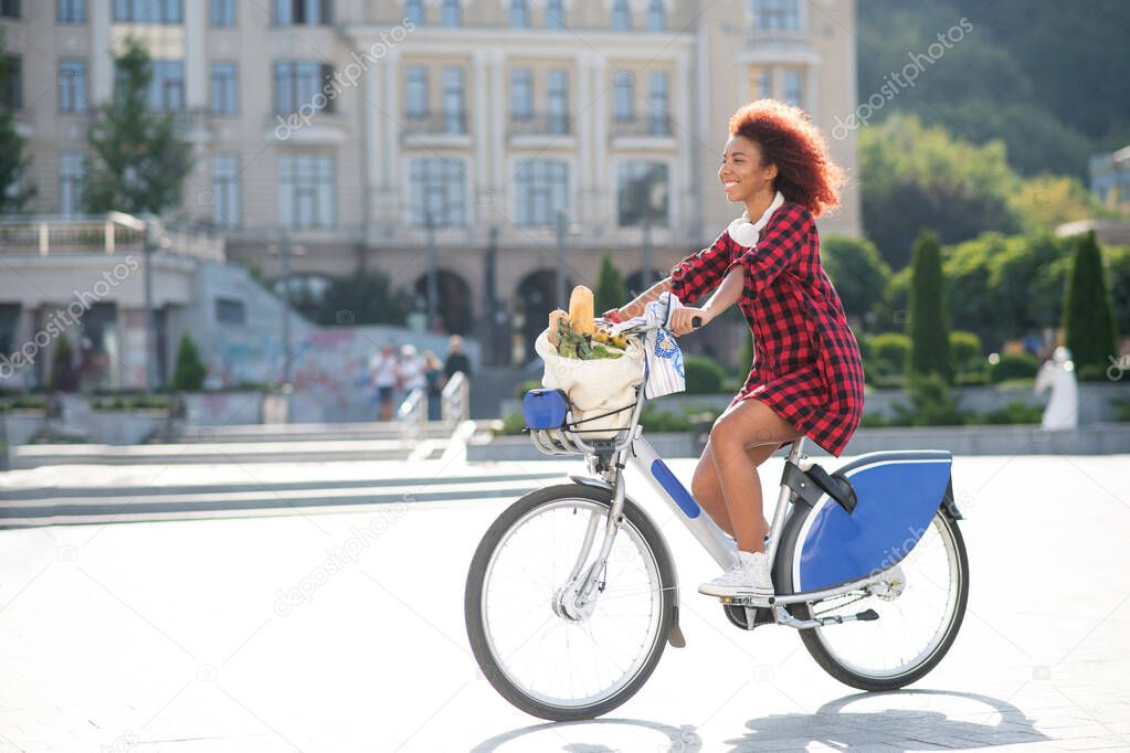 Curly red-haired woman riding bike after going to supermarket