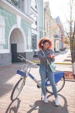 Akıllı saate bakıyorsun. Kot pantolon giyen kıvırcık öğrenci akıllı saate bakıyor. Bildirimleri kontrol ediyor.