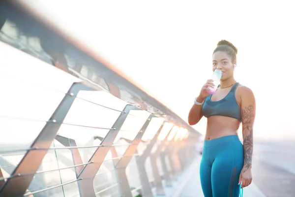 Mujer con polainas bebiendo agua después de hacer ejercicio afuera — Foto de Stock