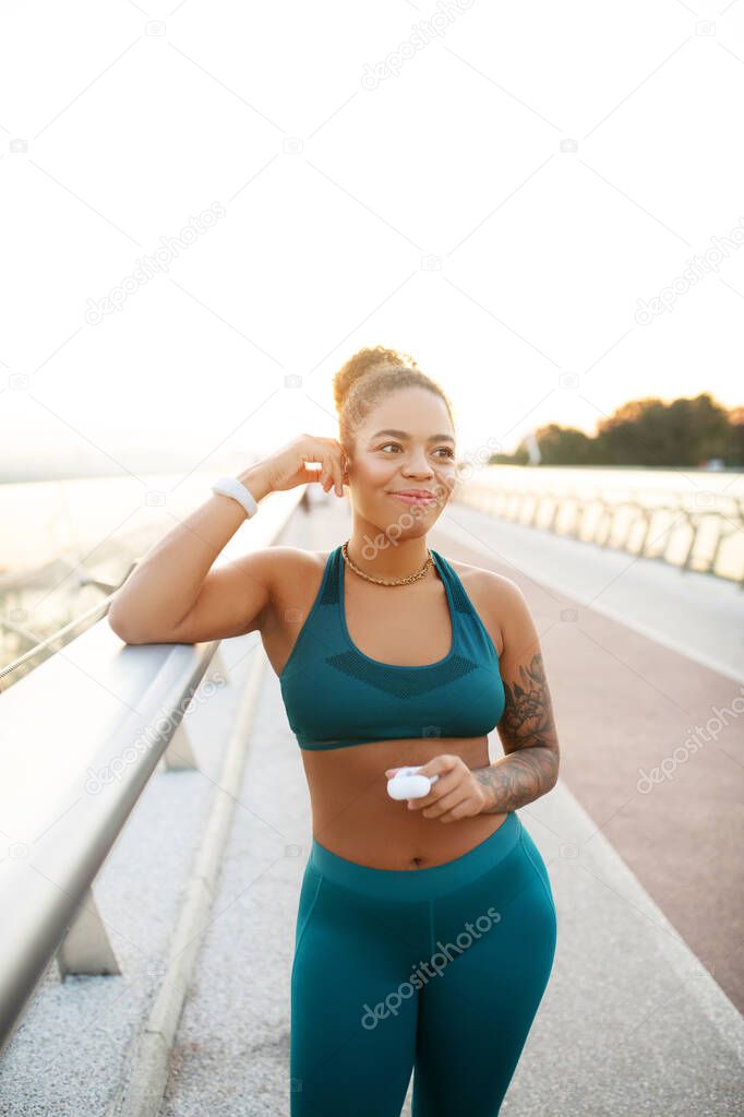Dark-skinned young woman putting earphones into ear