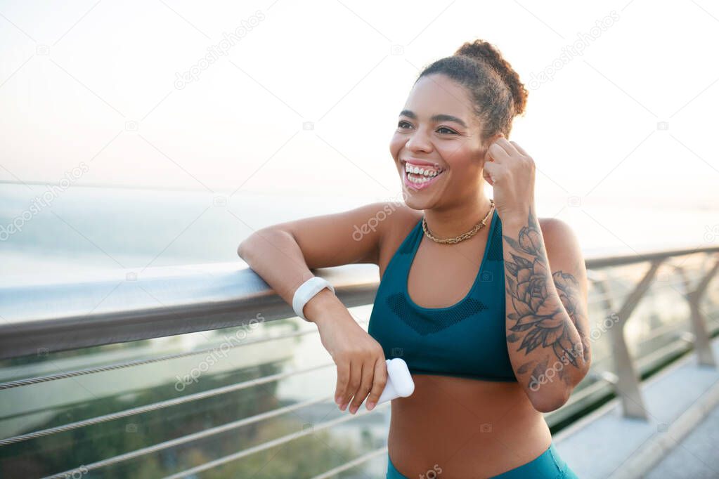 Beaming woman with nice tattoo on arm listening to music