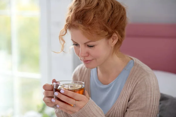 Kıvırcık hasta kadın sıcak çay içerken kendini iyi hissediyor. — Stok fotoğraf