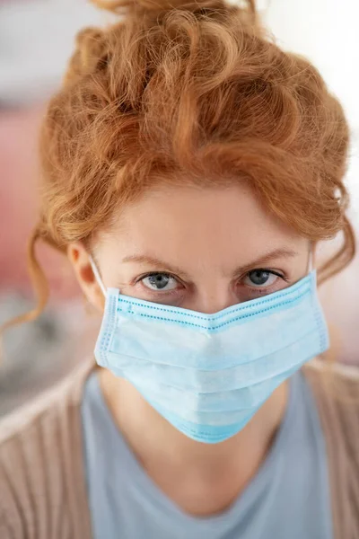 Femme malade aux yeux bleus avec des cheveux bouclés portant un masque de protection — Photo