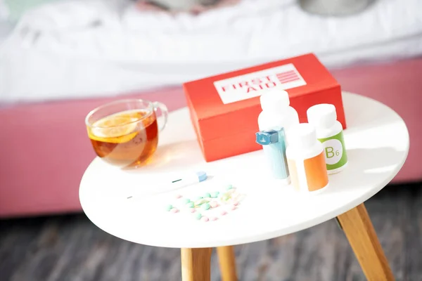 First aid kit and packs of pills standing near cup of tea