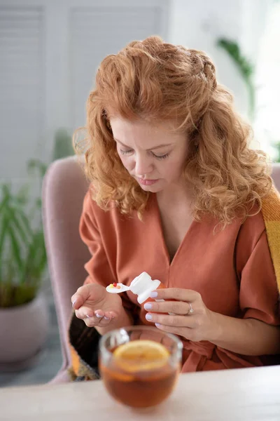 Кудрявая женщина принимает таблетки и пьет горячий чай с холодом — стоковое фото