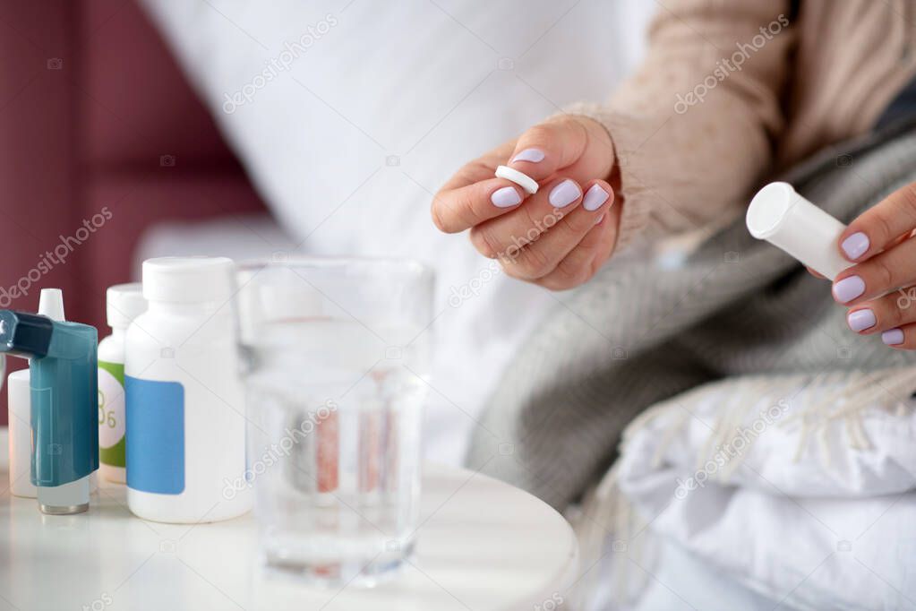 Woman with nice nail art holding pill while being on sick leave