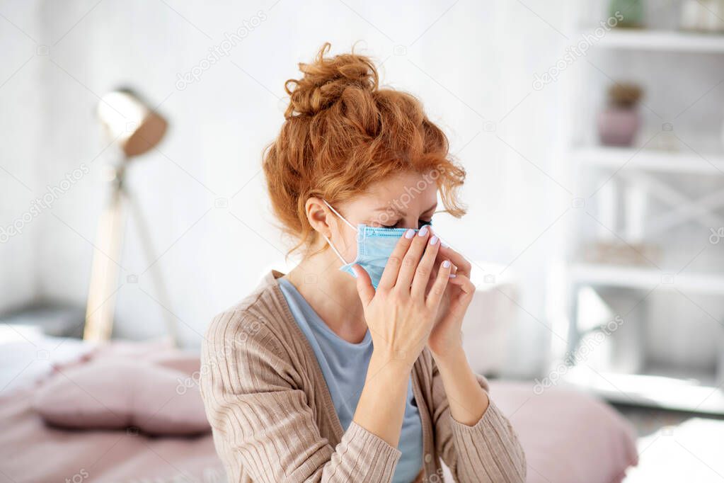 Curly woman sneezing after putting protective mask on