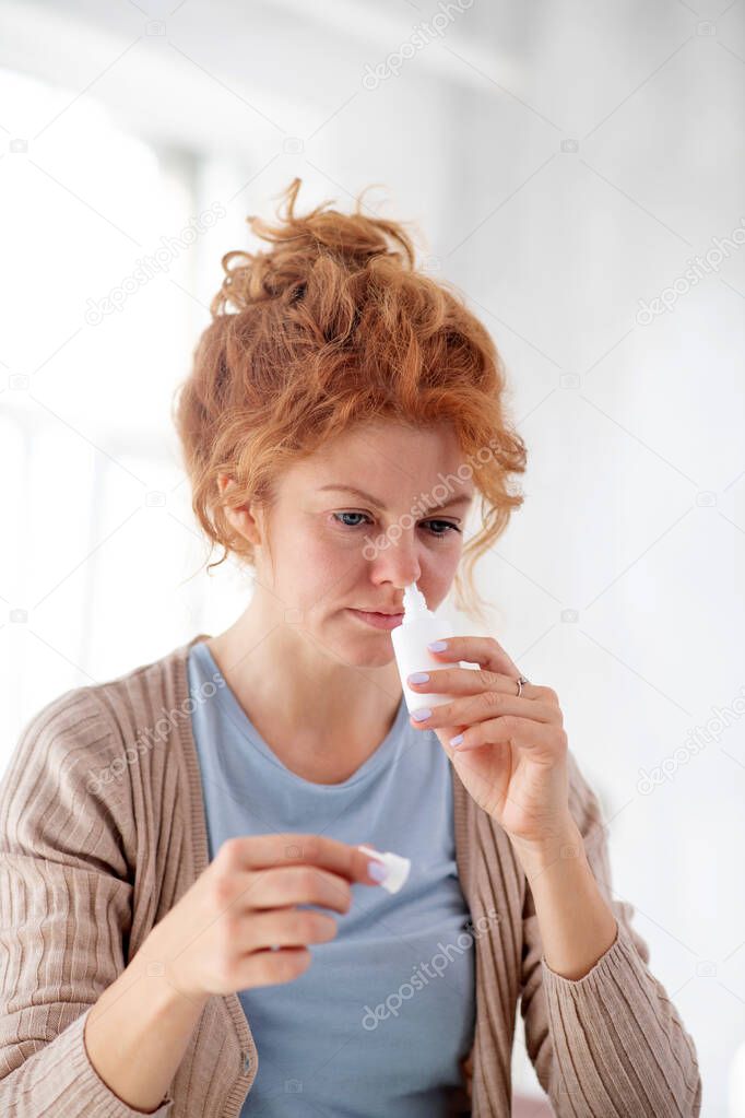 Woman taking nasal spray while having unbearable sneezing