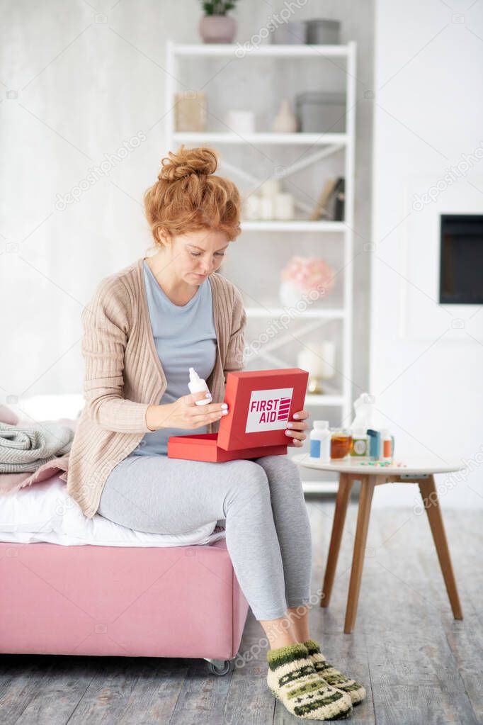 Woman holding first aid kit while suffering from cold