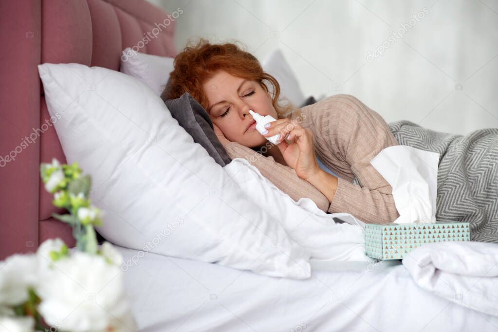Woman lying in bed with napkins and nasal spray