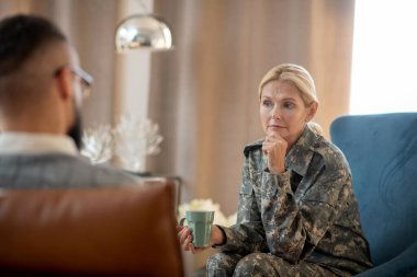 Kamuflaj üniforması giyen bir kadın psikanalistle konuşuyor.