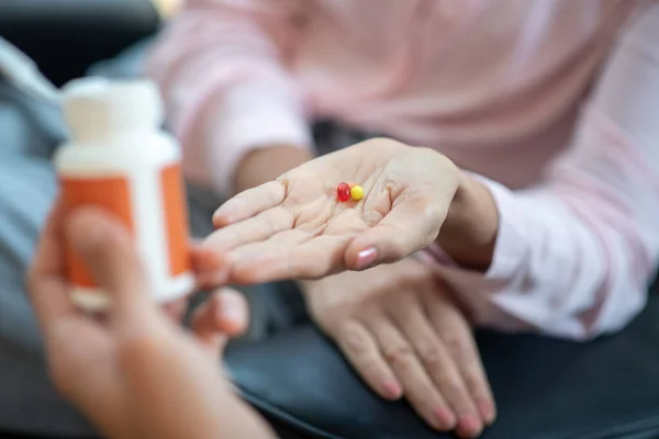 Donna che indossa camicetta rosa avendo pillole sul palmo della mano — Foto Stock