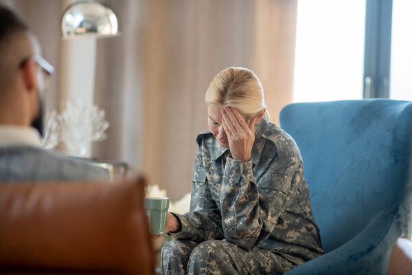 Blonde military woman having headache while remembering stressful events