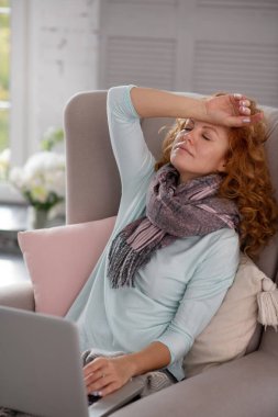 Baş ağrısı çeken bir kadın koltukta oturuyor.