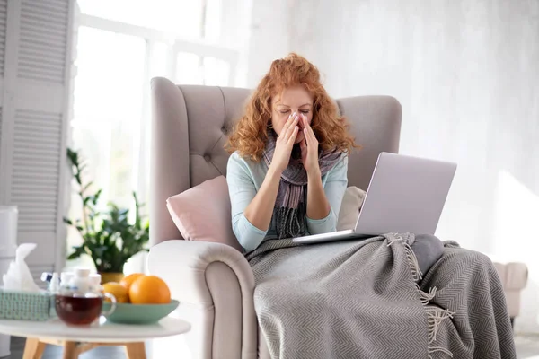 Rödhårig kvinna som sitter i fåtölj med laptop — Stockfoto