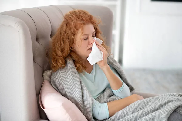 Nő ül karosszékben és tüsszögés miatt influenza — Stock Fotó
