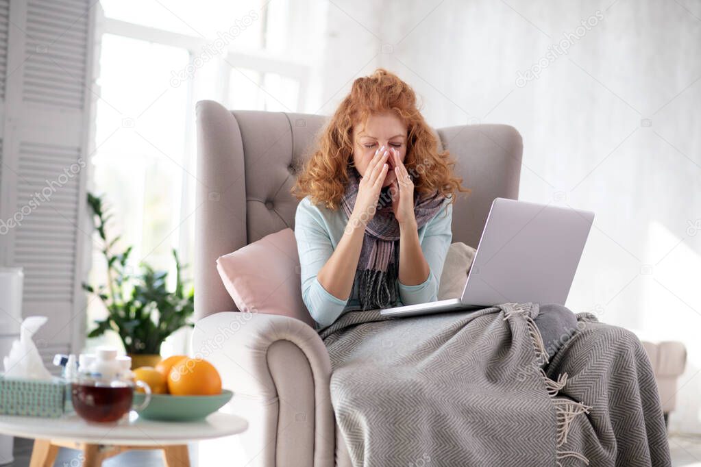 Red-haired woman sitting in armchair with laptop