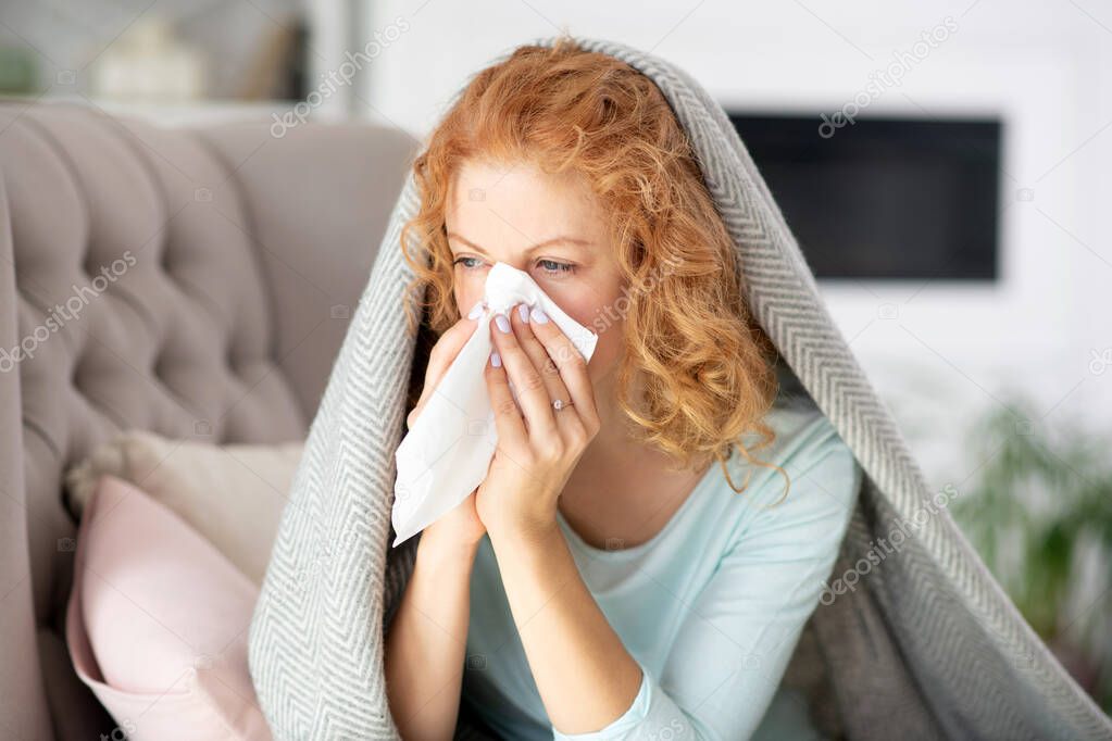 Sick woman sitting in the living room and sneezing