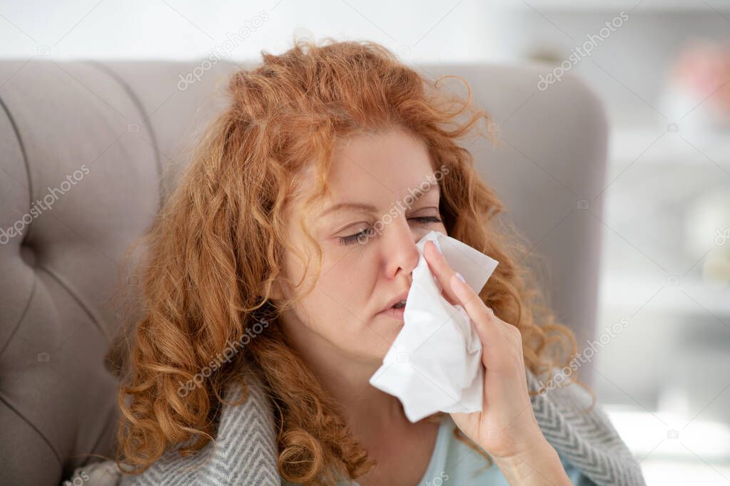 Curly woman on sick leave spending all day at home and sneezing
