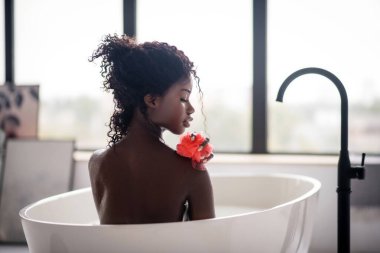 Kıvırcık esmer kadın banyo yaparken lifi tutuyor.
