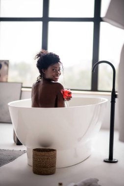 Banyo yaparken ve banyo lifi tutarken gülümseyen kadın.