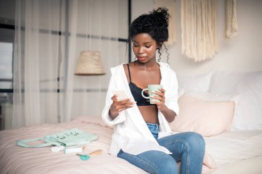 Mesajları okurken elinde beyaz akıllı telefon tutan esmer bir kadın.