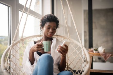 Kıvırcık kadın e-posta okurken oturup kahve içiyor.