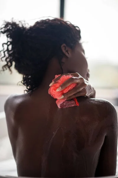 Lockige dunkelhaarige Frau benutzt Schleife, während sie ihren Rücken reinigt — Stockfoto