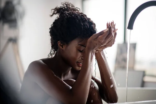 Кудрявая женщина с каплями воды на лице во время мытья — стоковое фото