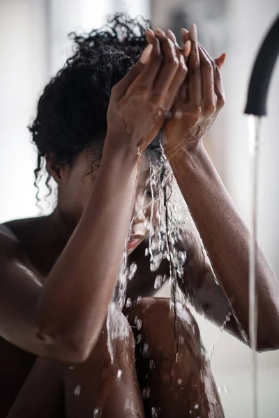 Dunkelhäutige junge Frau wäscht Gesicht, während sie in der Badewanne sitzt — Stockfoto