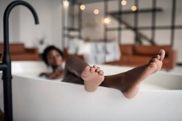 Close up of feet of young dark-skinned woman chilling in bath — ストック写真