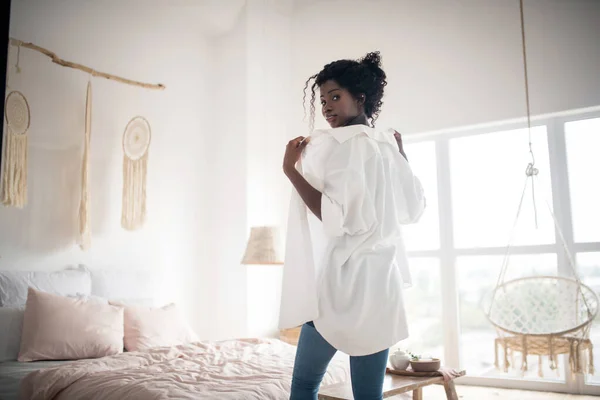 Curly woman wearing jeans putting white blouse on — ストック写真