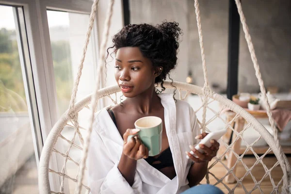 Curly woman looking into window while enjoying coffee