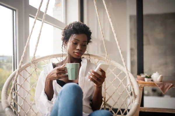 Kudrnatá žena sedí a pije kávu při čtení e-mailu — Stock fotografie