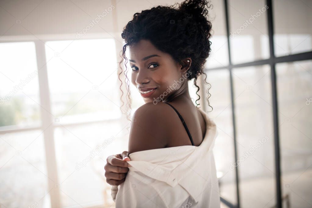Curly dark-haired woman smiling while dressing up