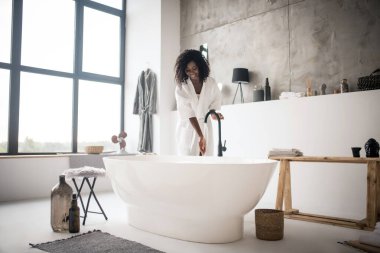 Kıvırcık güzel kadın köpüklü banyo yapmadan önce heyecanlanıyor.