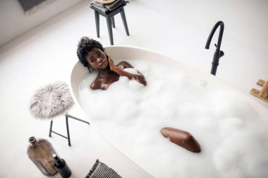 Dark-skinned woman feeling good while having bath clipart