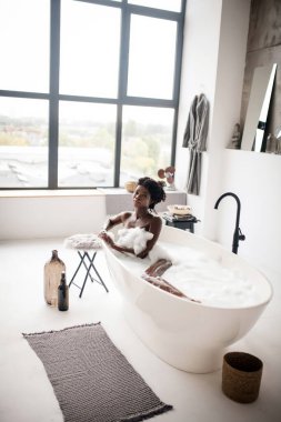 Çıplak, koyu tenli bir kadın köpüklü bir banyo yaptığı için iyi hissediyor.