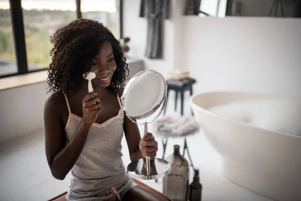 Krullende vrouw op zoek in spiegel terwijl het reinigen van haar huid — Stockfoto